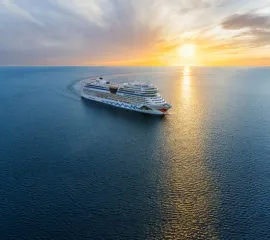 AIDAmar im Sonnenuntergang auf dem Meer, Ansicht von seitlich vorne, Fahrtrichtung von links nach rechts