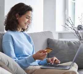 Eine Frau sitzt auf dem Sofa und bucht auf dem Laptop eine AIDA Kreuzfahrt auf Ahoi-Schiff.de.