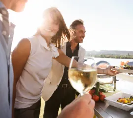 Eine Frau und zwei Männer genießen Essen und Wein an  Bord eines A-ROSA Flusskreuzfahrtschiffes.