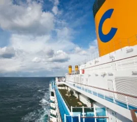 Die Seite der Costa Deliziosa auf offenem Meer. Zu sehen ist der Schornstein mit dem Costa Logo sowie eine begrünte Fläche auf dem Deck.