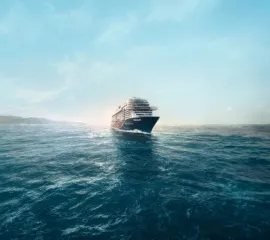 Ein Schiff der <i>Mein Schiff®</i>-Flotte von TUI Cruises auf offener See. Das Schiff wird von hinten durch die Sonne beleuchtet.