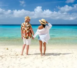 Ein Pärchen in Badekleidung steht am Strand und  schaut auf das Meer.