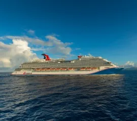 Die Carnival Vista in Seitenansicht auf dem offenen Meer. In Hintergrund sind vereinzelnte Wolken und Sonnenschein.