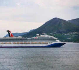 Die Carnival Liberty in Seitenansicht vor einer bergigen Landschaft im Meer.