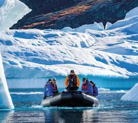Ein Zodiac Boot mit einem Reiseleiter von Hapag-Lloyd Cruises und vier Passagiere fahren durch die Eisberge und Gletscher in der Arktis.