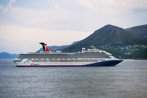 Ein Carnival Freedom Schiff gleitet im tiefblauen Wasser, im Hinterdrund sind  Gebirge zu sehen.