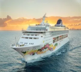 Das Schiff Norwegian Sky gleitet im tiefblauen Wasser während Sonnenaufgang.