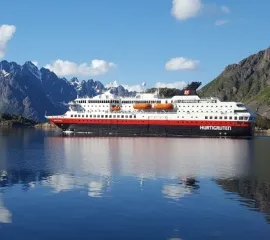 Die MS Nordnorge in einem norwegischen Fjord vor Berglandschaften unter blauem Himmel.