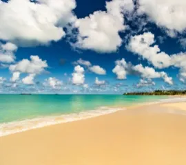 Karibischer Strand am türkisfarbenen Meer unter blauem Himmel mit weißen Wölkchen.