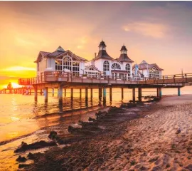 Strand an der Ostsee bei Sonnenuntergang mit Pfahlbauten im Vordergrund.