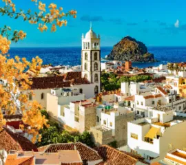 Eine sonnenbschienene Innenstadt auf einer Kanareninsel mit dem blauen Ozean im Hintergrund.