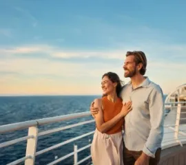 Ein paar steht auf dem Außendeck der Mein Schiff Flow. Sie haben ihre Kreuzfahrt mit Frühbucher-Vorteil gebucht.