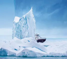 Eins von Hapag-Lloyd's Expeditionsschiffen vor einem großen Eisberg am Tag.