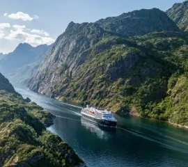 Ein Schiff der Havila Voyages Flotte fährt durch einen norwegischen Fjord.