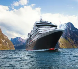 Die Queen Victoria im hohen Norden, während einer Fjordpassage. Das imposante Kreuzfahrtschiff ist von schräg vorne fotografiert und im Hintergrund sind steile Klippen und Berge zu sehen.