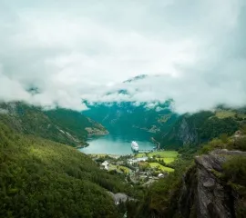 Ein Kreuzfahrtschiff im Geirangerfjord an einem bewölkten Tag. Sie möchten sich allgemein über Kreuzfahrten informieren? Dann finden Sie in diesem FAQ alle Antworten.