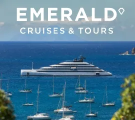 Die Yacht Emerald Kaia vor einer Küste neben vielen kleinen Booten. Logo Emerald Cruises & Tours.