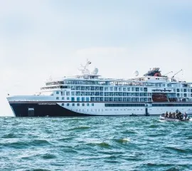 Die HANSEATIC inspiration von Hapag-Lloyd Cruises auf offener See in der Seitenansicht. Ein Zodiac mit Passagieren führt auf das Schiff zu.