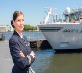 Eine Reiseleiterin von Amadeus, die vor einem Schiff der Flotte steht, das an einem Pier liegt.