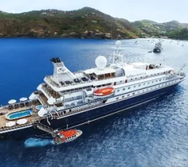 Die SeaDream I von SeaDream Yacht Club vor einer bergigen Küste im Wasser.