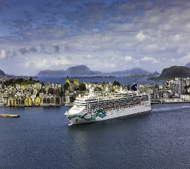 Ein beeindruckendes Schiff der Norwegian Cruise Line Flotte im tiefblauen Wasser eines europäischen Hafens unter leicht bewölktem Himmel.