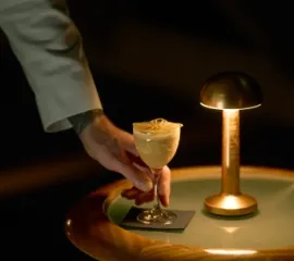 Eine Hand stellt eine Eiskreation auf einem Beistelltisch mit einer goldenen Lampe ab. Copyright: Max Emanuelson