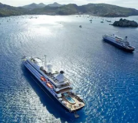 Die SeaDream I und SeaDream II vor einer felsigen Küste an einem sonnigen Tag.