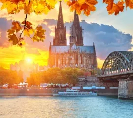 Der Kölner Dom und die Hohenzollernbrücke umrahmt von herbstlichen Bäumen im Sonnenuntergang.