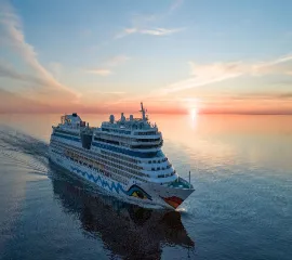 Ein AIDA Schiff auf hoher See, während im Hintergrund malerisch die Sonne versinkt.