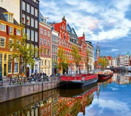 Bunte, historische Häuser an einer Gracht in Amsterdam. Am Ufer ankert ein kleines Boot.