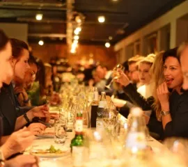 Personen auf einer Eventkreuzfahrt von nicko cruises sitzen an einer Tafel und essen en 5-Gänge-Menü von einem Sternekoch.