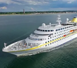 Die MS Hamburg der Reederei Plantours vor einer Küste mit flachem Land und tiefblauem Wasser.