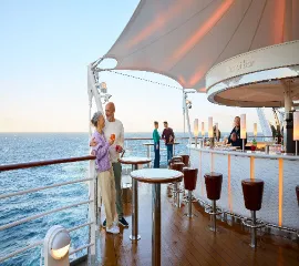 Ein älteres Pärchen, das an Deck steht und einen Drink an der Bar genießt.