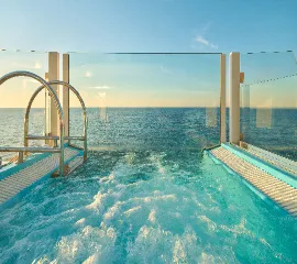 Sprudelnder Whirlpool auf dem Außendeck der Costa Favolosa mit gläserner Reling und freiem Blick über den weiten Ozean bei Sonnenuntergang.