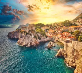 Die geschichtsträchtige Stadt Dubrovnik, fotografiert von ihrer Bucht aus, während eines spektakulären Sonnenuntergangs über den Dächern der Stadt.