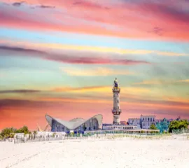 Der historische Warnemünder Leuchtturm und der markante Teepott am breiten, feinsandigen Ostseestrand unter einem farbenfrohen Abendhimmel – ideal für einen Landausflug auf eigene Faust.