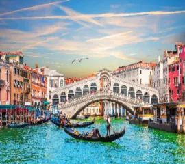 Traditionelle Gondeln auf dem smaragdgrünen Canal Grande vor der historischen Rialtobrücke in Venedig bei sanftem Abendlicht.