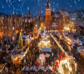 Festlich beleuchteter Weihnachtsmarkt in einer historischen Altstadt bei nächtlichem Schneefall mit Karussell und Marktständen – ein Highlight während einer Flusskreuzfahrt in der Adventszeit.