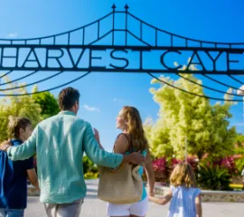 Eine Familie läuft unter dem großen, schwarzen Eingangstor mit dem geschwungenen Schriftzug „Harvest Caye“ auf der tropischen Privatinsel in Belize.