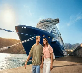 EIn glückliches Pärchen, das Händchenhaltend vor der Mein Schiff Relax läuft.