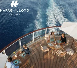Gäste beim exklusiven Freiluft-Dining auf dem Holzdeck eines Hapag-Lloyd Cruises Luxusschiffs mit Blick auf das Meer.