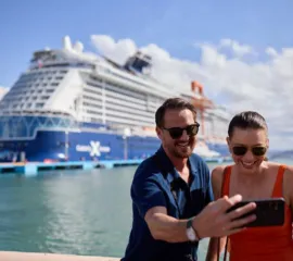 Einn Paar schaut sich auf dem Smartphone ihre Clubpunkte an und freuen sich vor einem Schiff von Celebrity Cruises.