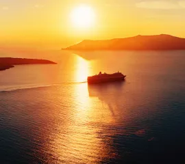 Ein Kreuzfahrtschiff fährt im gelben Sonnenuntergang entlang kleiner Inseln.