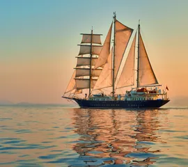 Ein Segelschiff schippert im Sonnenuntergang durch das sanfte Wasser.