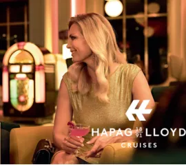 Eine elegante Dame mit Cocktail und ein Herr im Anzug genießen die Abendstimmung in der Lounge an Bord von Hapag-Lloyd Cruises.