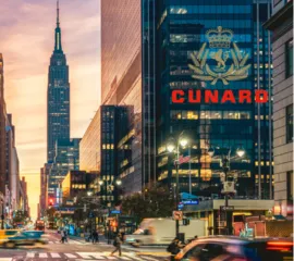 Blick entlang einer belebten Straße in Manhattan mit dem Empire State Building in der Abenddämmerung und dem goldenen Cunard Logo für das Arrangement The New Yorker.