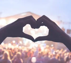 Feiernde Menschen bei einem Konzert. Eine Person formt aus den Händen ein Herz.