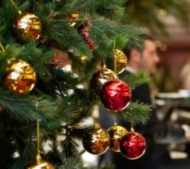 MSC Weihnachtsbaumkugeln an einer frischen Tanne in der Lobby eines MSC Schiffes. Im Hintergrund spielt ein Mann Klavier.