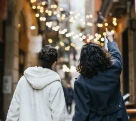 Zwei Personen mit dunklen Haaren stehen mit dem Rücken zur Kamera und schauen sich Lichter in der Stadt an.