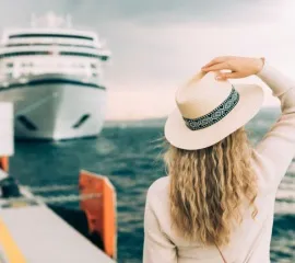 Reisende steht an Land und blickt auf großes Kreuzfahrtschiff.